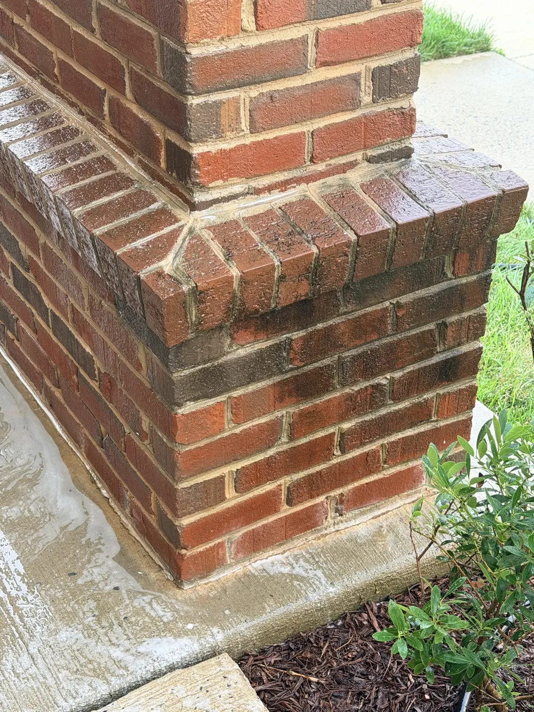 A brick entry column stained dark with algae and dirt in the mortar lines, before cleaning.