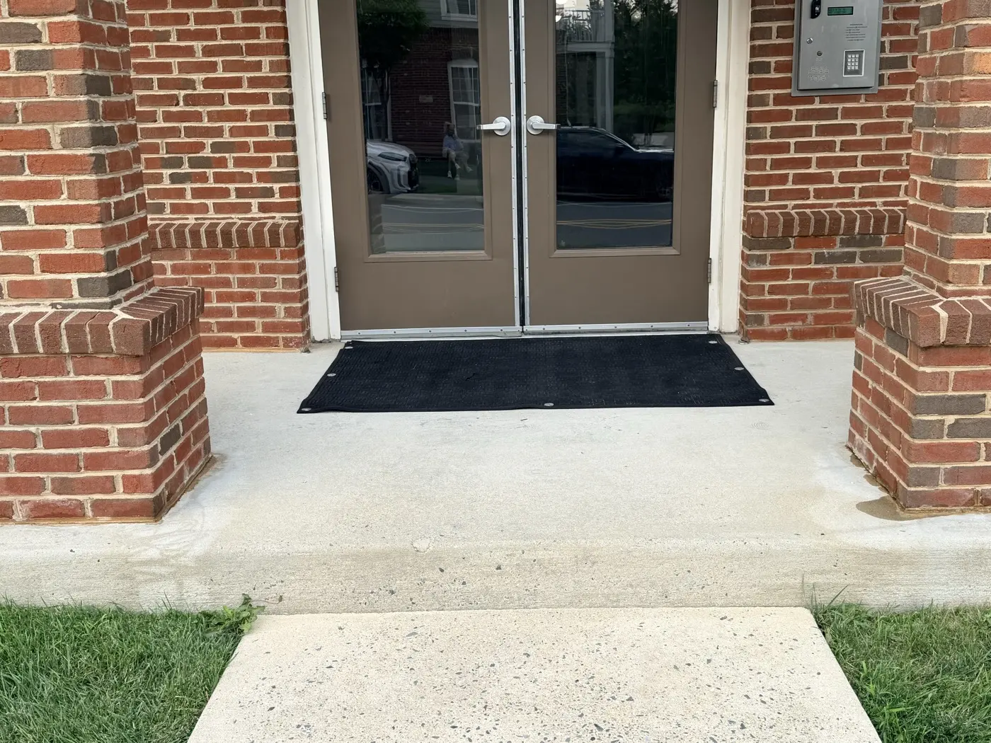 A cleaned commercial entryway: bright concrete walkway, washed brick columns, and a clear glass door.