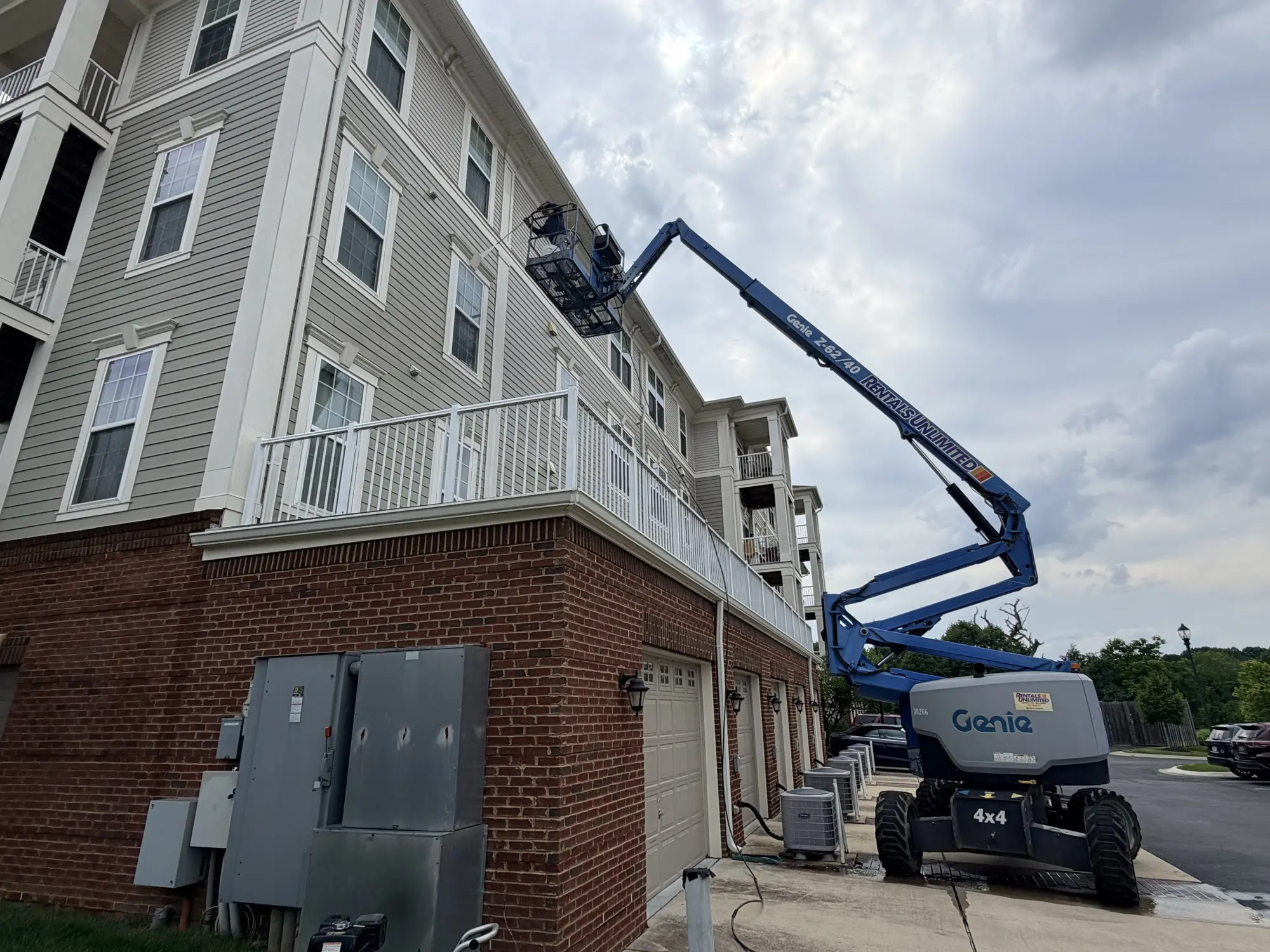 A Signature technician on a boom lift soft washing the upper floors of a four-story brick and siding building.