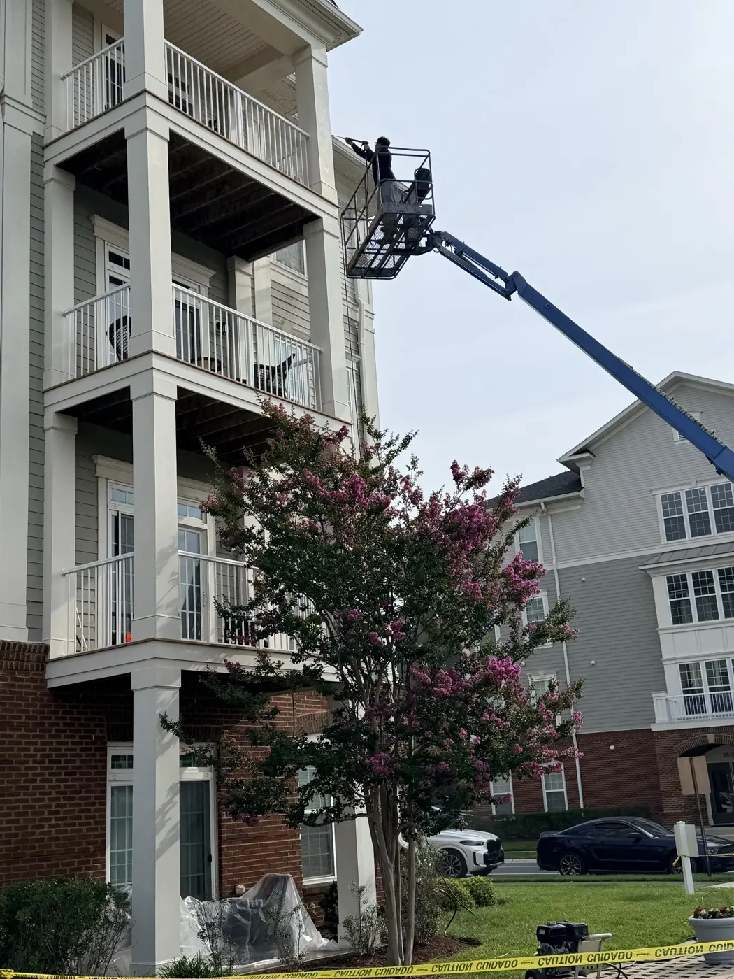 A technician on a boom lift washing balcony ceilings and siding on a four-story residential building.